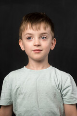A thoughtful 7-year-old in a light blue t-shirt, black chalkboard backdrop. Represents childhood, education, and creativity for academic or lifestyle concepts.