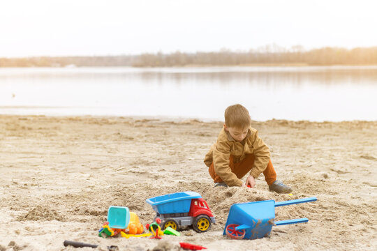 A child playing with colorful toys on a sandy beach near a calm lake, enjoying a sunny day outdoors. Perfect for concepts of childhood, playtime, and nature.
