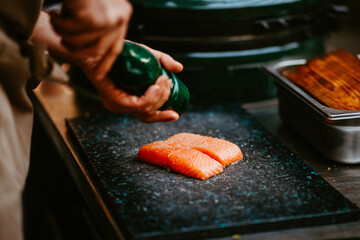 chef's hands seasoning salmon fillets with pepper by grill.