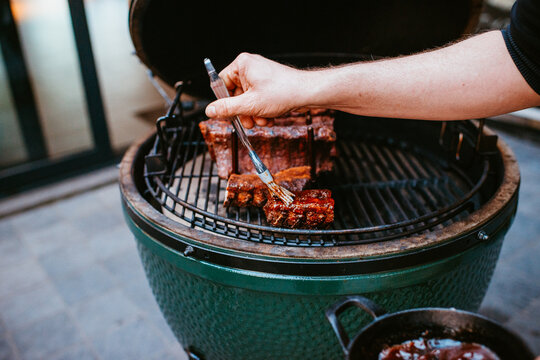 person basting ribs with sauce on green ceramic grill outdoors