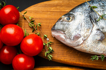 Raw dorado fish on a wooden cutting board with oregano and cherry tomatoes. Close-up. View from above.