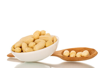 Roasted peanuts in a white ceramic saucer and with a wooden spoon, close-up, isolated on a white background.