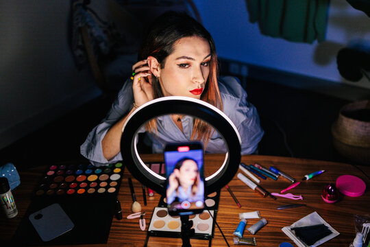 A person is filmed sitting at a table with makeup products