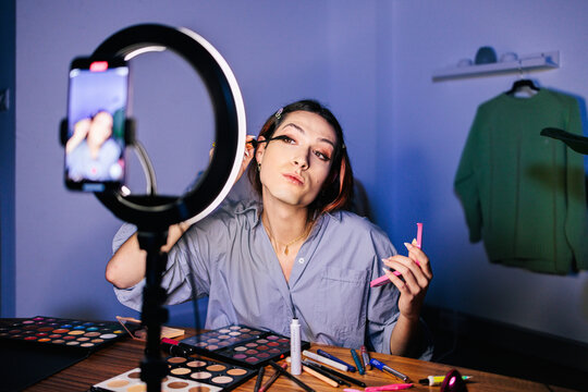 A person applies makeup using a mirror surrounded by a ring light