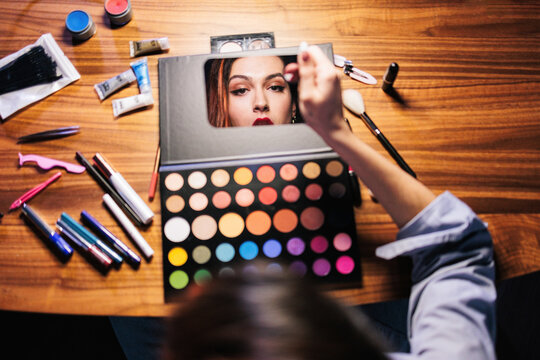 A person applies makeup using a colorful eyeshadow palette and brushes