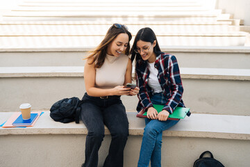 Cheerful students checking posts on social media with cellphone