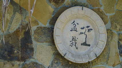 Rustic stone plate with bonsai art and Asian calligraphy hanging on a natural wall.