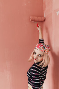 Woman painting pink wall at home