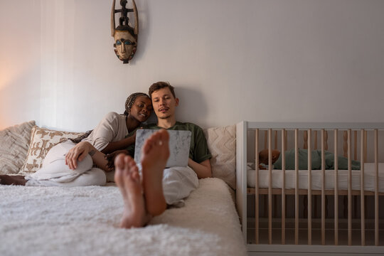Multiracial parents watching movie while newborn is sleeping