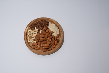 mix of nuts almonds and cashews and flax seeds and sesame seeds lie on a round wooden plate on a white background