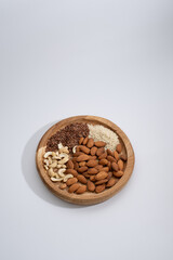mix of nuts almonds and cashews and flax seeds and sesame seeds lie on a round wooden plate on a white background
