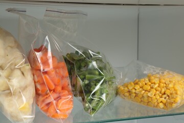 Plastic bags with different frozen vegetables in refrigerator, closeup