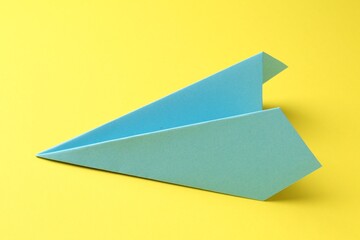 One handmade light blue paper plane on yellow background