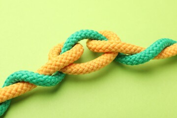 Colorful ropes tied in knot on green background, closeup. Unity concept
