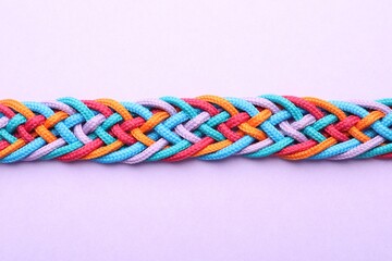 Braided colorful ropes on violet background, top view. Unity concept