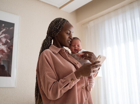 Modern mother holding baby and using smartphone
