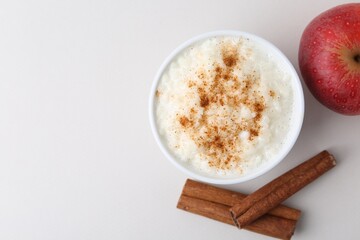 Delicious rice pudding with apple and cinnamon on light background, flat lay. Space for text