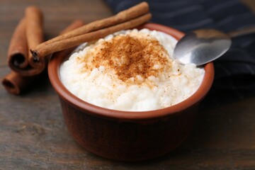 Delicious rice pudding with cinnamon sticks on wooden table, closeup