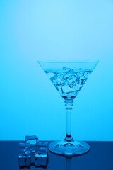 Cocktail glass with water and ice cubes on table, color tone effect