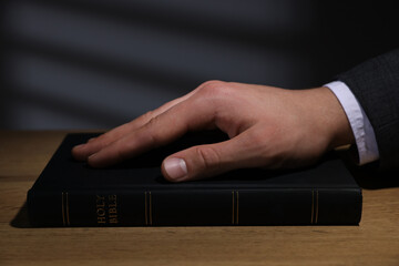Man taking oath with his hand on Bible at wooden table, closeup