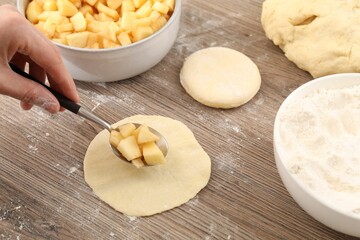 Woman making pirozhki (stuffed pastry pies) with apples at wooden table, closeup