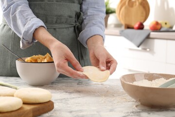 Woman making pirozhki (stuffed pastry pies) at white marble table indoors, closeup