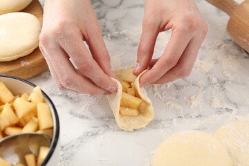 Woman making pirozhki (stuffed pastry pies) with apples at white marble table, closeup