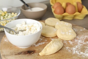 Making pirozhki (stuffed pastry pies). Pieces of dough with cottage cheese on table, closeup