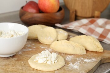 Making pirozhki (stuffed pastry pies). Pieces of dough with cottage cheese on table, closeup