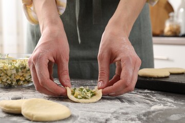 Woman making pirozhki (stuffed pastry pies) with eggs and dill at gray table indoors, closeup