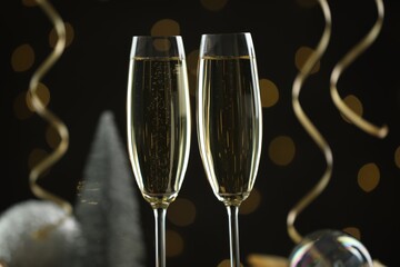 Delicious champagne in glasses and Christmas decor against black background with blurred lights, closeup