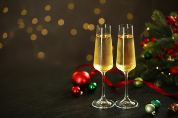 Delicious champagne in glasses and Christmas decor on grey table against blurred lights, space for text