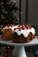 Traditional Christmas cake decorated with red currants and rosemary on table against blurred lights