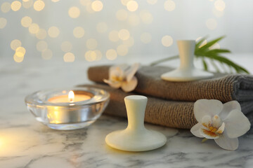 Spa stones, orchid flowers, towels and burning candle on white marble table, closeup