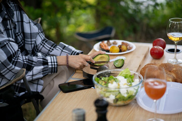 A person cuts vegetables on a wooden cutting board with a knife while preparing a salad outdoors