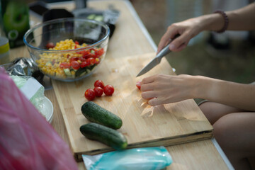 A person cuts vegetables on a wooden cutting board with a knife while preparing a salad outdoors