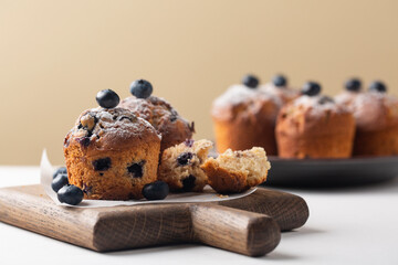Homemade blueberry muffins without muffins cup, on white table, decorated with fresh blueberries and powdered sugar.