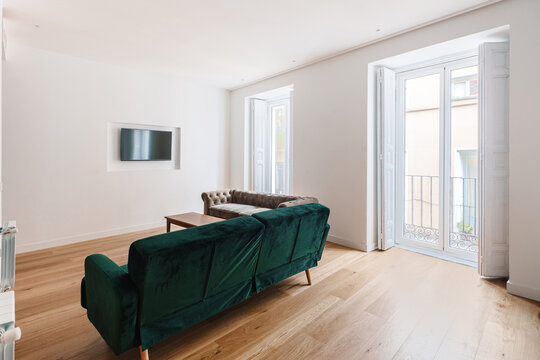 A minimalist living room with a green couch and a beige tufted sofa