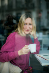 A portrait of a woman sitting in a café, holding a cup and a notebook, while a photographer's...