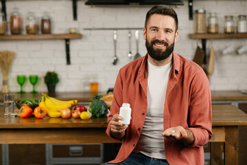 A man with a beard pours pills from a jar onto his hand and smiling. The concept of taking pills. Pills, vitamins, dietary supplements