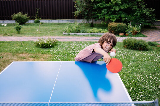 Young child playing table tennis in a sunny backyard garden.