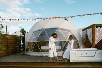 Relaxing women in spa robes near luxurious geodesic dome retreat