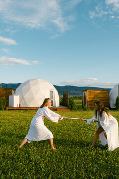Two women playfully sword fight at sunset while glamping