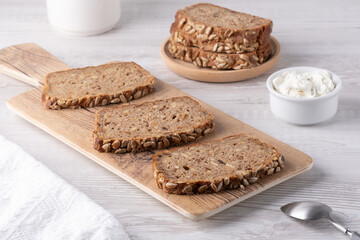 Freshly sliced whole grain bread served with cottage cheese on a rustic wooden board in a bright kitchen setting