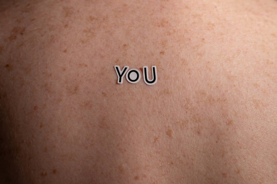 Close-up of the word You on freckled skin surface