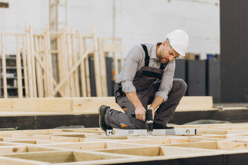 Carpenter using spirit level and screwdriver building wooden frame in workshop