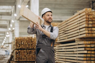 Carpenter carrying wooden plank in timber warehouse