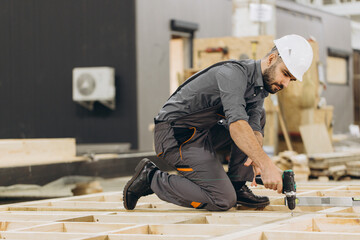 Construction worker building wooden frame for modular house using cordless drill