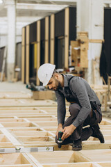 Carpenter using cordless drill assembling modular house in factory