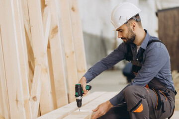 Carpenter using cordless drill assembling wooden frame in workshop